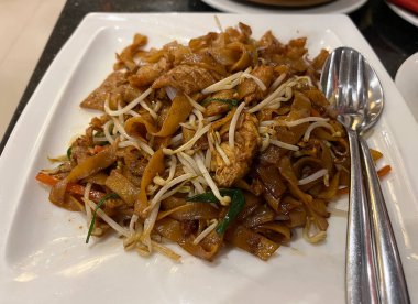 Kızarmış geniş pirinç eriştesi, soğan, fasulye filizi ve soya sosu.