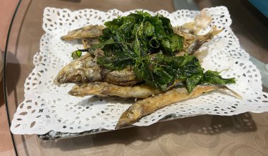 Kızarmış tuzlu küçük balık, üzerinde kızarmış fesleğen yaprakları var..