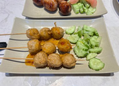 Şiş üzerinde kızartılmış karides topları, tatlı ve baharatlı sos serpiştirilmiş, dilimlenmiş salatalıkla servis edilmiş..