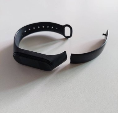 Yırtılmış ve zarar görmüş bir kayışı olan akıllı bir sağlık kol saati beyaz bir masanın üzerinde yatıyor..