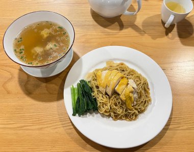 Haşlanmış tavuklu kuru erişte ve yanında çorba ile servis edilen kızarmış bok choy.