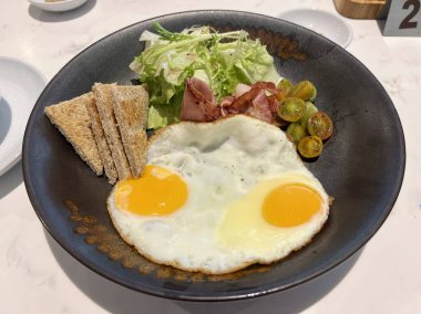 Kahvaltı seti bir salata, kızarmış ekmek ve iki kızarmış yumurta içeriyor.