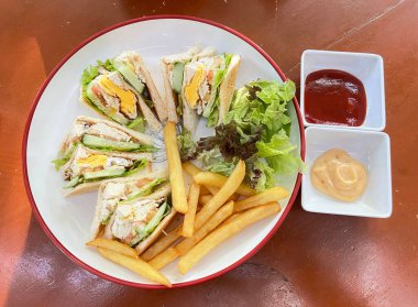 Kahvaltı setinde yumurtalı sandviç, patates kızartması, ketçap ve mayonezden yapılmış sos var..