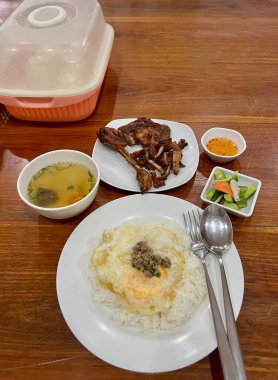 Üzerine kızarmış yumurta ve ızgara tavuk, yanında çorba, sebze turşusu ve tatlı ve baharatlı sosla servis edilmiş pilav.