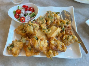 Taze biber, dilimlenmiş arpacık soğanı ve salatalık dilimlerinden yapılan sos ile servis edilen çıtır çıtır ezilmiş sesbania çiçekleri..