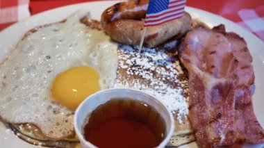 Krep, yumurta, pastırma, sosis ve üstünde küçük bir Amerikan bayrağı olan bir Amerikan kahvaltısı.