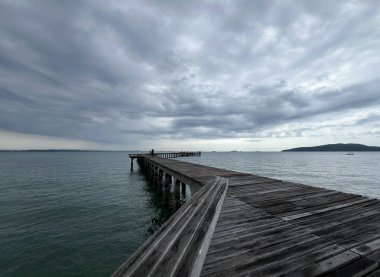 Bir turist, Rayong 'daki rıhtımdan sakin deniz meltemiyle çevrili olarak balık tutmayı sever.
