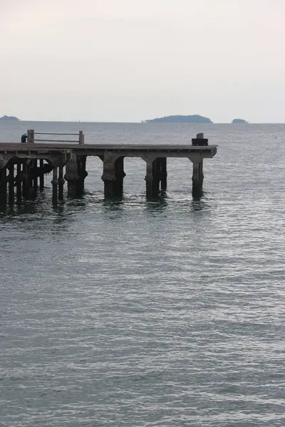 Bir turist, Rayong 'daki rıhtımdan sakin deniz meltemiyle çevrili olarak balık tutmayı sever.