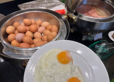 Sıcak suda tutulan haşlanmış yumurta ve jambon dilimleri, açık büfe masasında servis edilir.