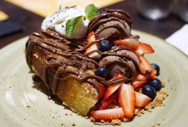Zengin çikolatalı dondurmayla servis edilen meyveli ekmek pudingi.
