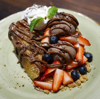 Zengin çikolatalı dondurmayla servis edilen meyveli ekmek pudingi.