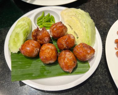 Salatalık, lahana ve taze biberle servis edilen Tayland usulü sosis.