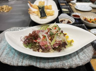 Maguro Tataki 'nin eritme tabağı Tayland baharatlı bitki salatası, üzerinde yosun ve taze bitkiler var.