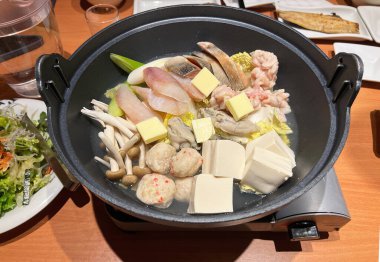 Taze deniz ürünleri, sebzeler ve soya peyniri Japon usulü bir sukiyaki kabında haşlandı.