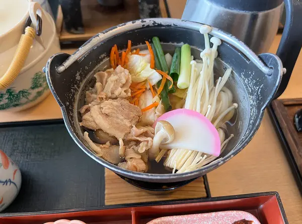 Dilimlenmiş domuz eti, taze sebze ve mantarlı Udon erişteleri geleneksel bir Japon demir tenceresinde servis edilir.