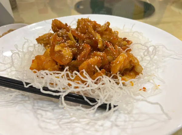 Susam yağı soslu kızarmış karides, çıtır erişteyle servis edilir.