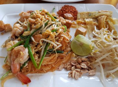 Kızarmış Tayland eriştesi, taze karides, kavrulmuş fıstık ve limon dilimleri..