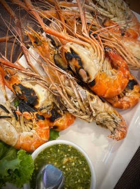 Izgara nehir karidesleri, baharatlı deniz ürünleri sosuyla servis edilir..