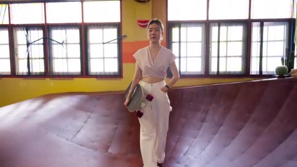 女性は自信を持って スケートボードを手に歩く 屋内スケート 彼女は興奮と可能性の約束を運ぶ スタイルと汎用性のシンボル 高品質4K映像 — ストック動画