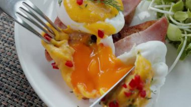  Benedict yumurtası zarifçe kırılmış ve içindeki leziz sarıyı ortaya çıkarmış. Zengin, altın sarısı, bu klasik yemeğe cazibe katarak, kadifemsi bir lezzet patlaması vaat ediyor. Yüksek kalite 4k görüntü