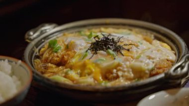 Katsu Don 'un dramatik ışığı: Japon mutfak klasiğinin baştan çıkarıcı bir görüntüsü, yoğun ve gölgeli aydınlatma ile yıkanmış. Baharatlı sosta kaynatılmış pirzola. Yüksek kalite 4k görüntü