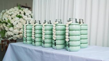 Üzerinde beyaz çiçek çelengi olan yeşil yemek kutusu gelenek ve estetiğin bir birleşimi. Canlı yeşil tiffin, süslenmiş taze beyaz çiçek çelengi, güzelliği temsil ediyor. Yüksek kalite 4k görüntü