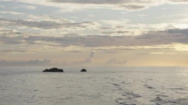 Uçsuz bucaksız okyanusta, vanilya gökyüzü ve bulutlu renklerle çevrili küçük bir ada. Doğal dram, sakin bir adanın olduğu büyüleyici bir manzarada yaşanıyor. Yüksek kalite 4k görüntü