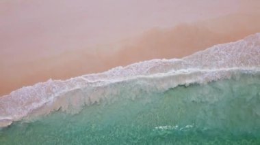 İnsansız hava aracından gelen hava görüntüleri büyüleyici bir görüntü sunuyor, temiz dalgaların el değmemiş beyaz kumsala çarpmasıyla kıyıdan uzaklaşıyor. Sahne, okyanusun kıyılarla buluşmasının dinamik güzelliğini yakalar.