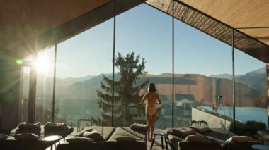 Zarif beyaz mayo giymiş bir kadın görkemli dağ manzarasına karşı gevşiyor. Sofistike ve sakin bir atmosferle, dinginliği somutlaştırıyor. Yüksek kalite 4k görüntü