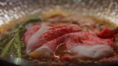 A5 et dilimlerini gümüş bir kapta, sukiyaki çorbasıyla yakın plan, mermer dokuya ve lezzetli çorbaya vurgu yapıyor. Bifteğin kalitesini ve lezzetini göstermek için mükemmel..