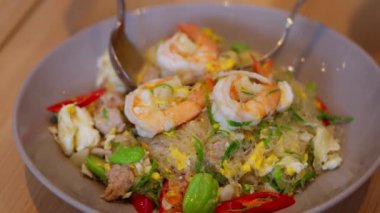 Lezzetli karideslerle kaplanmış Tayland eriştesi. Canlı renkler ve taze malzemeler sergileniyor. Tuzlu, aromatik tatların ve çekici sunumun vurgulanması. Yüksek kalite 4K görüntü