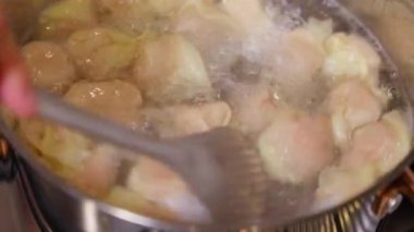 Kaynar suda hamur köftelerinin karıştırılmasının yakın çekim görüntüleri, yükselen buhar ve fokurdayan hareketler yaratıyor. Bu otantik yemek sahnesi geleneksel mutfak hazırlama süreci, aşçılık videoları.