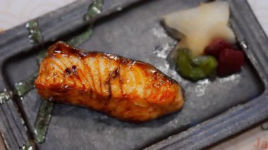 Japon somon bifteği aperatifinin yakın çekimi, mükemmel bir şekilde altın kabukla kurutulmuş ve narin otlarla süslenmiş. Zarif tabaklarda servis edilen bu yemek tazeliği ve zarafeti ön plana çıkarıyor..