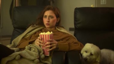 Güzel beyaz kadın, köpek patlamış mısırı yerken ve beslerken korku filmi seyrediyor, sonra sıçrıyor ve patlamış mısırı döküyor. ARRI Alexa ile ArriRaw 'da çekildi ve QuickTime Apple ProRes 422 HQ ihraç edildi..