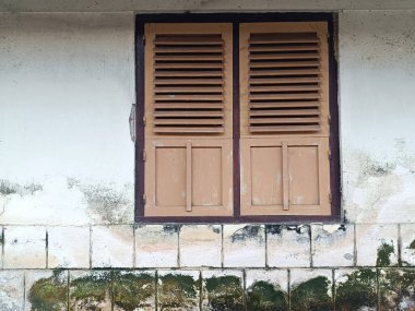 Altında ızgara ve paneller olan eski bir ahşap pencere. Endonezya 'da eski, yosunlu bir bina..