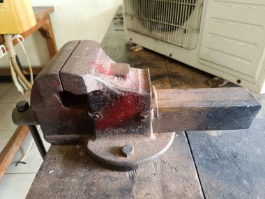 Bir atölyedeki ahşap tezgahta paslı bir bank mengene. Metal veya ahşap işçiliği için endüstriyel el aletler.