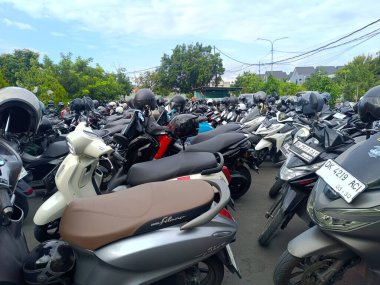 Bali, Endonezya - 26 Ağustos 2025: Denpasar şehir bölgesindeki ağaçların ve binaların arka planında gün boyunca çeşitli marka ve modellerden oluşan kalabalık bir motosiklet parkı atmosferi.