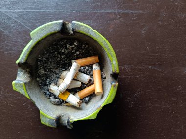 Ahşap masada sigara izmaritleri ve kül dolu yeşil kırık kül tablası..