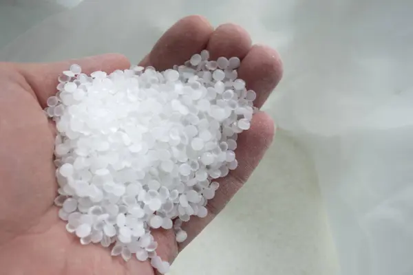 Elinde şeffaf beyaz polietilen granüller var.