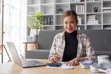 Çekici Asyalı kadın serbest yazar projesini planlıyor, oturma odasındaki kahve masasında dizüstü bilgisayarında çalışıyor....