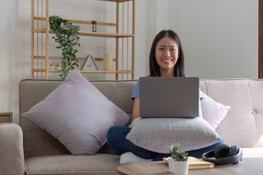 Çekici, genç, mutlu bir kadın. Oturma odasında kulaklıkla müzik dinliyor. Kanepeye uzanıyor, dizüstü bilgisayar kullanıyor ve dinleniyor....