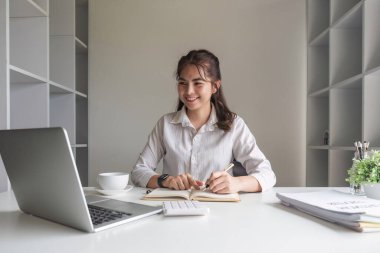 Dizüstü bilgisayar ve hesap makinesiyle çalışan iş kadını, mali danışmanı analiz ediyor, istatistik raporu hazırlıyor, belgeleri inceliyor, iş kadını mali tabloları denetliyor ve kısa grafikler yazıyor.