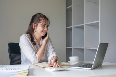 Çalışkan iş kadını, patronuyla telefonda konuşurken bütçeyi analiz etmek için hesap makinesi kullanıyor....