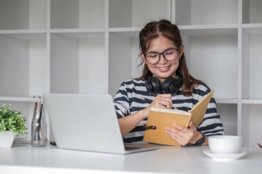 Asyalı kız öğrenci çevrimiçi sınıfta çalışıyor, çevrimiçi çalışıyor, kulaklık takıyor, video izliyor, zumluyor, bilgisayarlı dizüstü bilgisayarla mutlu Asyalı kadın öğrenme dili öğreniyor...