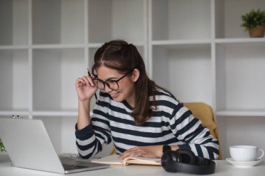 Asyalı kız öğrenci çevrimiçi sınıfta çalışıyor, çevrimiçi çalışıyor, kulaklık takıyor, video izliyor, zumluyor, bilgisayarlı dizüstü bilgisayarla mutlu Asyalı kadın öğrenme dili öğreniyor...