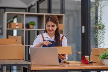 Küçük işletme girişimcisi KME, kutuda kumaş paketleyen Asyalı kadın. Portre genç Asyalı küçük işletme sahibi ev sahibi, çevrimiçi satış pazarlama teslimatı, KME e-ticaret tele pazarlama kavramı.