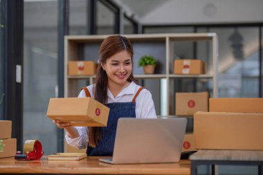 Startup small business entrepreneur SME, asian woman packing cloth in box. Portrait young Asian small business owner home office, online sell marketing delivery, SME e-commerce telemarketing concept.