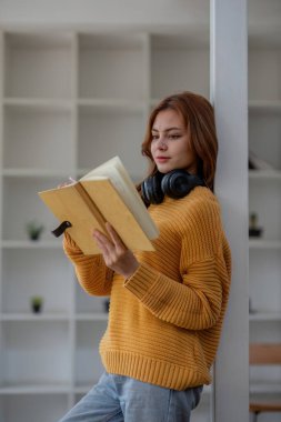 Okul kütüphanesinde elinde fotokopi kitabı tutarak gülümseyen kız öğrenci evden uzaktan ev ödevini internetten hazırla..