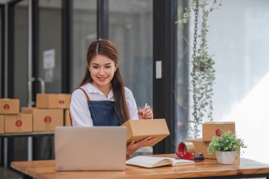 Küçük işletme girişimcisi KME, kutuda kumaş paketleyen Asyalı kadın. Portre genç Asyalı küçük işletme sahibi ev sahibi, çevrimiçi satış pazarlama teslimatı, KME e-ticaret tele pazarlama kavramı.