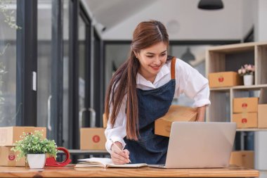 Küçük işletme girişimcisi KME, kutuda kumaş paketleyen Asyalı kadın. Portre genç Asyalı küçük işletme sahibi ev sahibi, çevrimiçi satış pazarlama teslimatı, KME e-ticaret tele pazarlama kavramı.